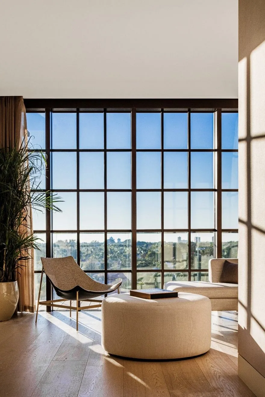 Elegant lounge with floor-to-ceiling grid windows overlooking a cityscape at golden hour.